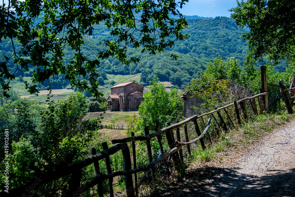 Una iglesia prerrománica se asoma en un camino en las montañas cubiertas de bosques y prados con vallas de madera en la región española de Asturias