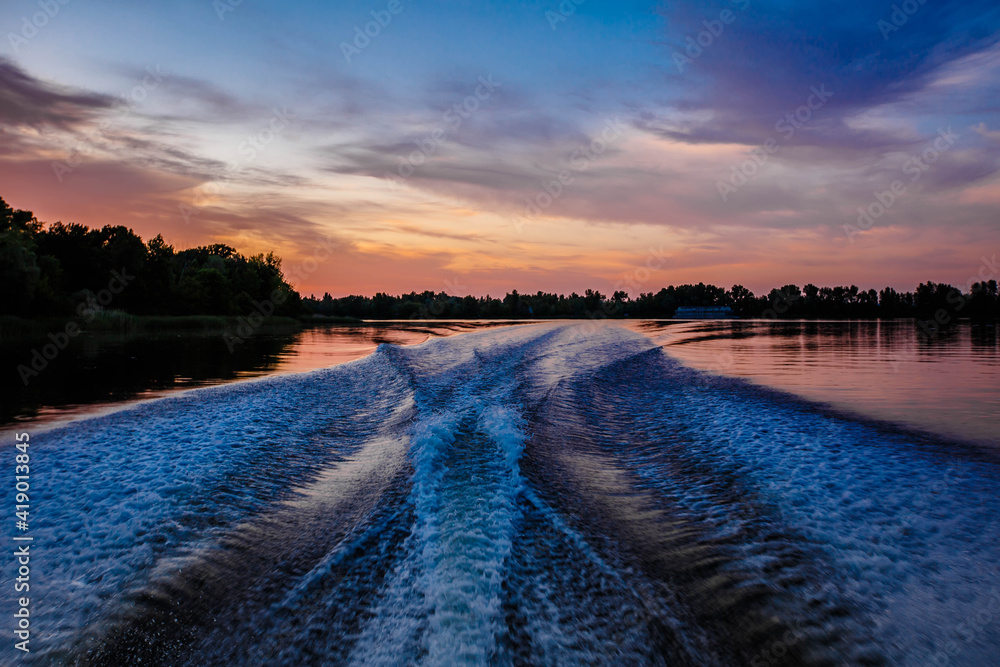 Deep river. Evening. Moving from coast to coast. A very beautiful path through the water behind the stern of the boat from the engine.
