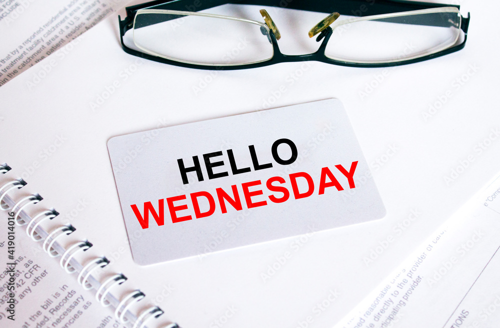 Text Hello Wednesday on a business card lying on a notepad with eyeglasses and text documents Text Hello Wednesday on a business card lying on a notepad with eyeglasses and text documents