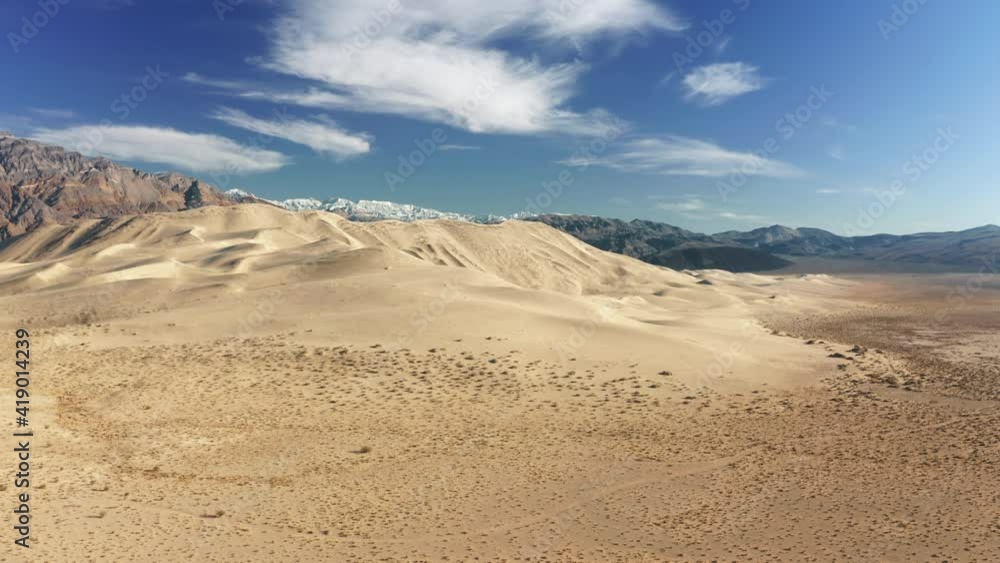 Drone rising up above golden dune hill under blue sky on sunny winter day. Scenic mountain landscape, desert nature 4K shot. Sand dunes aerial with high snow summit and cloud in blue sky on background Drone rising up above golden dune hill under blue sky on sunny winter day. Scenic mountain landscape, desert nature 4K shot. Sand dunes aerial with high snow summit and cloud in blue sky on background