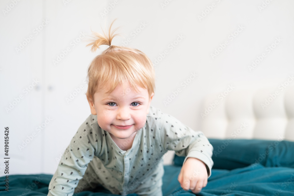 Fototapeta premium Little funny toddler boy in pajamas having fun in bed at home, green bedding