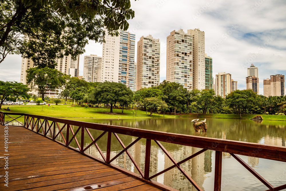 Fototapeta premium Lago no Parque Flamboyant, com prédios e céu com nuvens ao fundo em dias de lockdown.