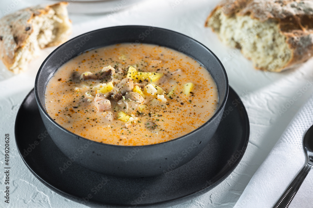 Cream cheese soup with mushrooms and potatoes, delicious first course in black bowl on the white table, top view horizontal Cream cheese soup with mushrooms and potatoes, delicious first course in black bowl on the white table, top view horizontal