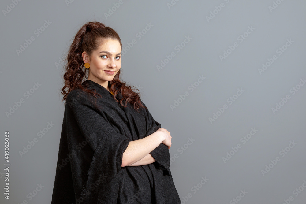 Fototapeta premium portrait of charming curly-haired woman in a black cloak isolated on a gray background