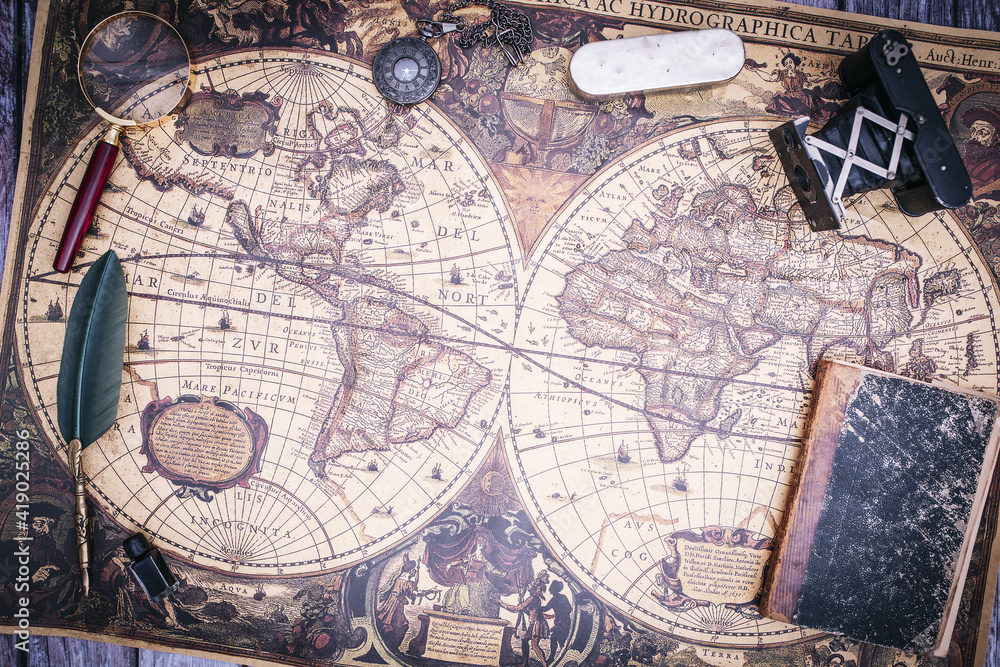Fototapeta premium zenithal view of still life composed of old books, pistols, pen with ink, camera and clock on a background of a classic map.