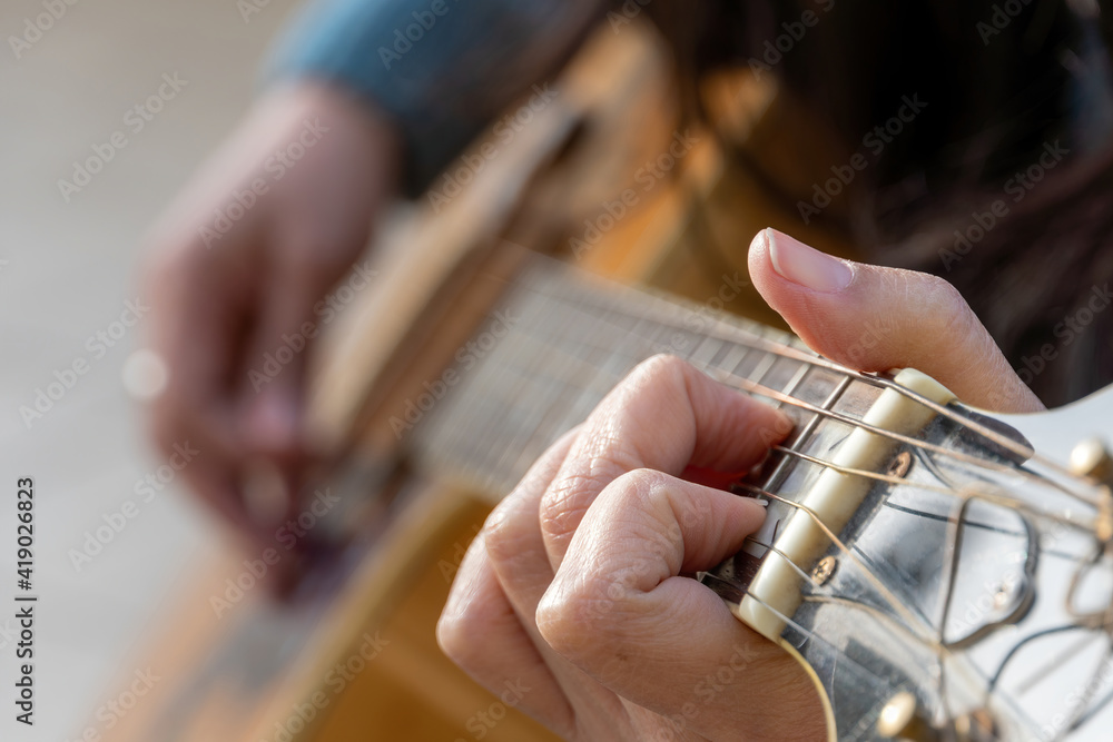 Unrecognized concentrated woman playing guitar outdoors. Selective focus.