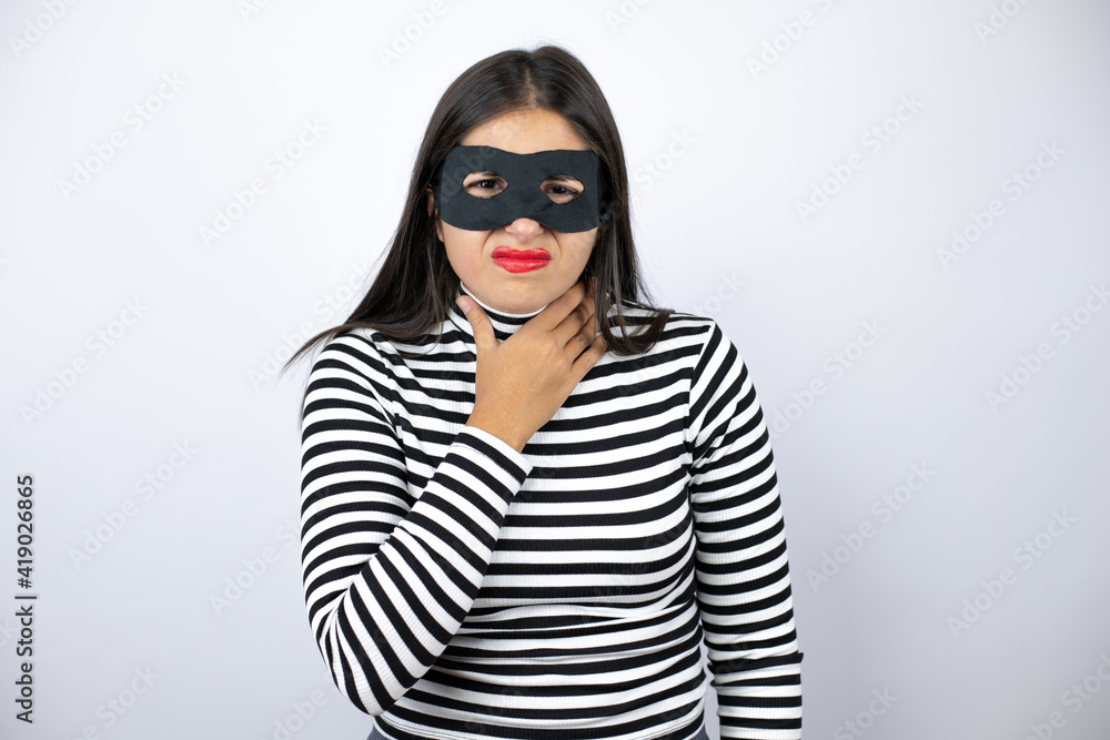 Young beautiful brunette burglar woman wearing mask painful neck, sore throat for flu, clod and infection Young beautiful brunette burglar woman wearing mask painful neck, sore throat for flu, clod and infection