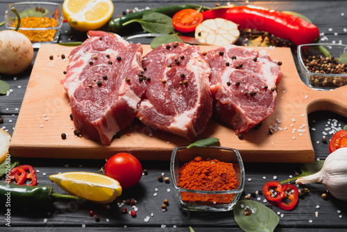 Raw pork meat on wooden cutting board at kitchen table for cooking pork steak roasted or grilled with ingredients herb and spices , Fresh pork