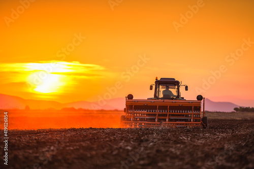 Beautiful sunset, farmer in tractor preparing land with seedbed cultivator