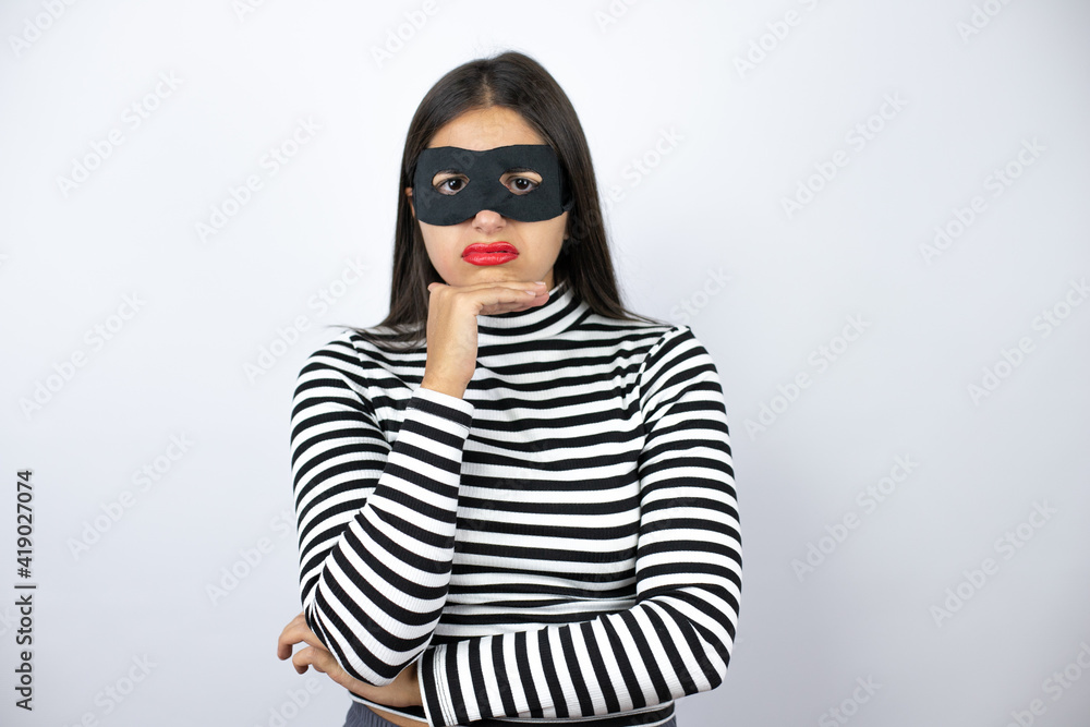 Young beautiful brunette burglar woman wearing mask thinking looking tired and bored with crossed arms Young beautiful brunette burglar woman wearing mask thinking looking tired and bored with crossed arms