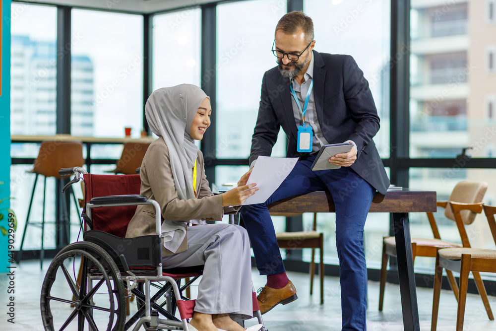 The manager is using the tablet while he is listening the female employee present the information of the report. Female muslim officer is sitting on the wheelchair and holding the document on hand. The manager is using the tablet while he is listening the female employee present the information of the report. Female muslim officer is sitting on the wheelchair and holding the document on hand.