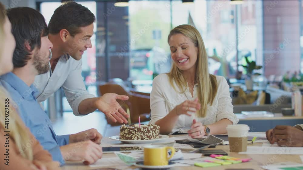 Colleagues celebrating businesswoman's birthday with cake and candle at meeting around table in modern open plan office - shot in slow motion Colleagues celebrating businesswoman's birthday with cake and candle at meeting around table in modern open plan office - shot in slow motion