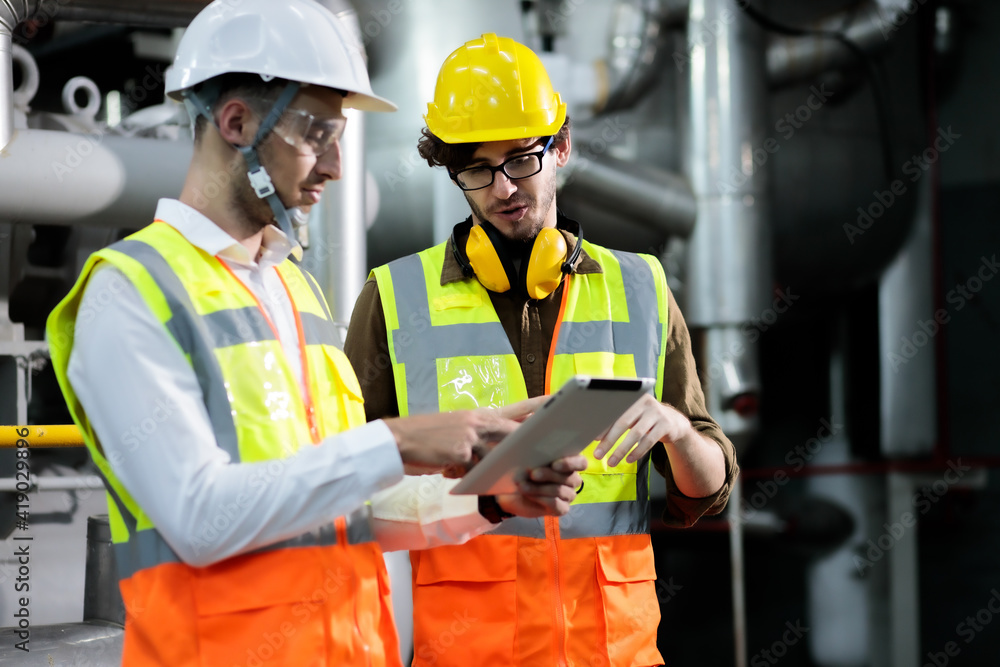 Two maintenance engineers discuss inspect relay checking machinery and repair system in a factory. They work a heavy industry manufacturing factory. Two maintenance engineers discuss inspect relay checking machinery and repair system in a factory. They work a heavy industry manufacturing factory.