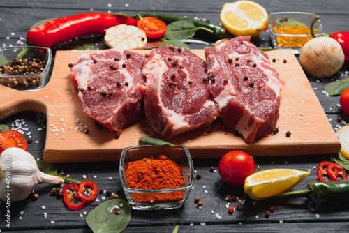 Raw pork meat on wooden cutting board at kitchen table for cooking pork steak roasted or grilled with ingredients herb and spices , Fresh pork