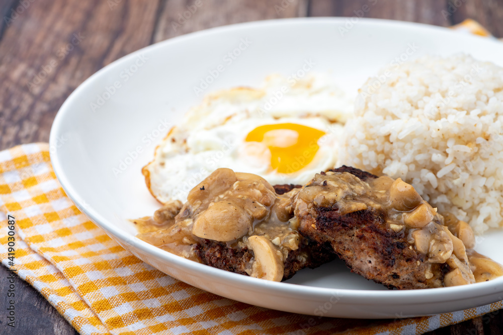Mushroom Burger Steak Silog (side shot close up)-is a famous Filipino meal that consists of burger steak covered in mushroom gravy sauce, egg and fried rice Mushroom Burger Steak Silog (side shot close up)-is a famous Filipino meal that consists of burger steak covered in mushroom gravy sauce, egg and fried rice
