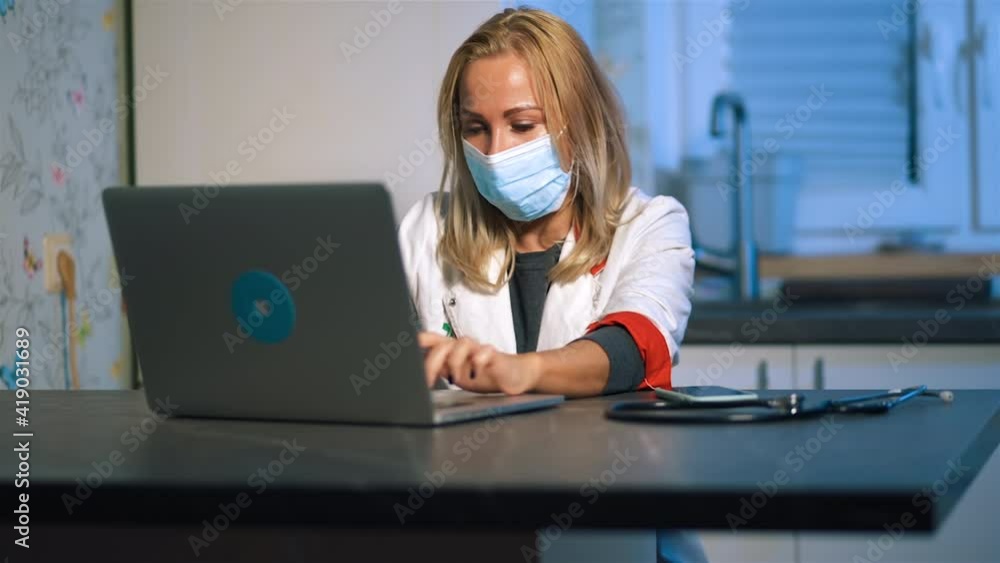 Modern female doctor in medical mask using laptop and phone during home visit Modern female doctor in medical mask using laptop and phone during home visit