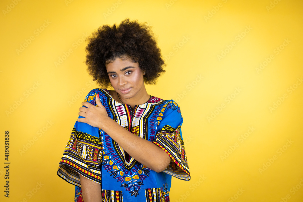 African american woman wearing african clothing over yellow background with pain on her shoulder and a painful expression African american woman wearing african clothing over yellow background with pain on her shoulder and a painful expression