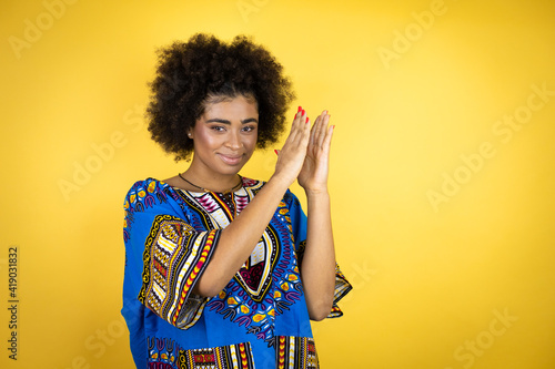 African american woman wearing african clothing over yellow background clapping and applauding happy and joyful, smiling proud hands together