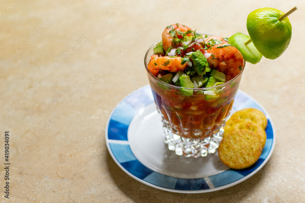 side view of a delicious shrimp cocktail with crackers, chopped onion, cilantro, avocado and lime, on a white plate with green. Fresh Mexican food side view of a delicious shrimp cocktail with crackers, chopped onion, cilantro, avocado and lime, on a white plate with green. Fresh Mexican food