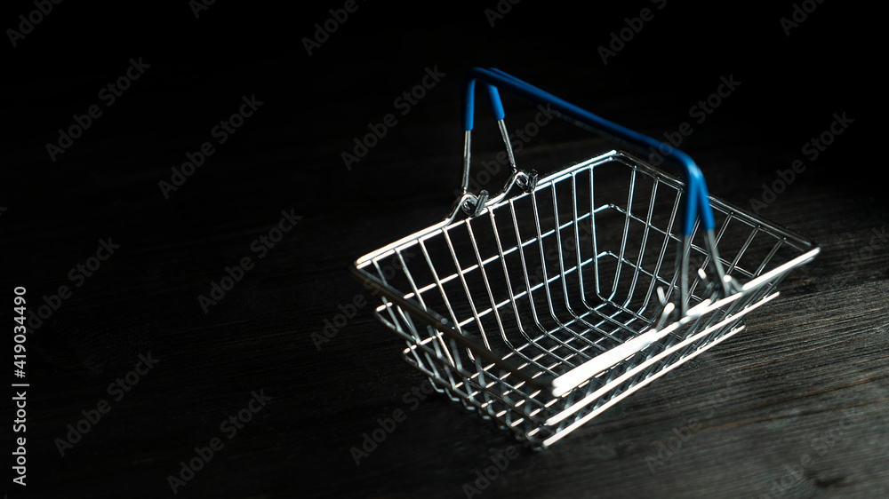 Empty mini toy self-service shopping basket with blue handles close up isolated on dark black background Empty mini toy self-service shopping basket with blue handles close up isolated on dark black background