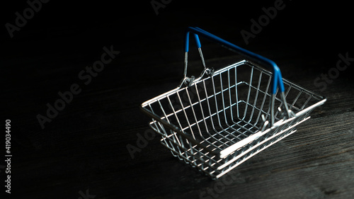 Empty mini toy self-service shopping basket with blue handles close up isolated on dark black background