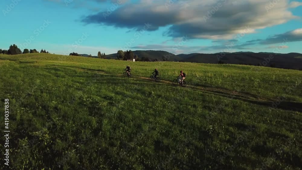 Closing in on mountain bikers on off road grass trail ascending up the hill. Aerial view of active people on bicycles on an outdoor track Closing in on mountain bikers on off road grass trail ascending up the hill. Aerial view of active people on bicycles on an outdoor track