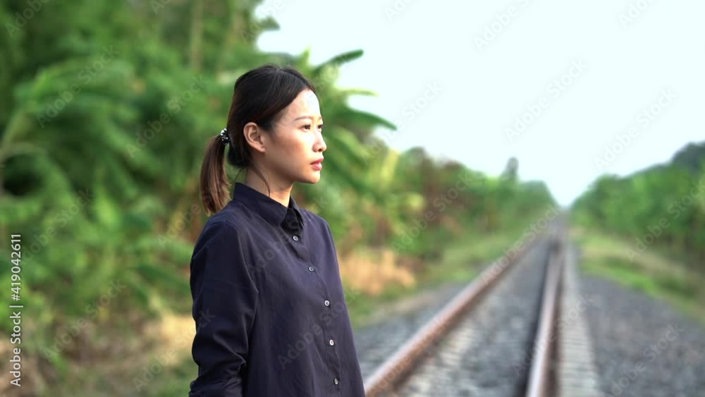 The young beautiful asian woman who tied the hair back wearing in black shirt and jean is walking and thinking about her life on the local railroad with banana trees forest in the sideway, then she st The young beautiful asian woman who tied the hair back wearing in black shirt and jean is walking and thinking about her life on the local railroad with banana trees forest in the sideway, then she st