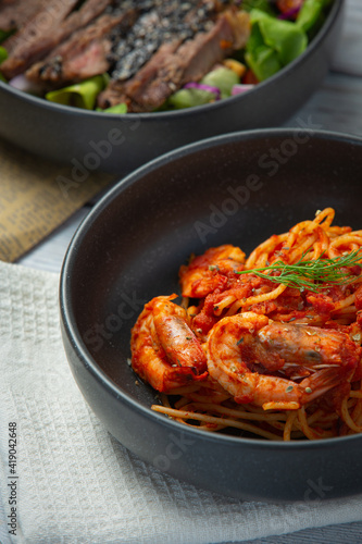 spaghetti with shrimps in tomato sauce on white wooden background