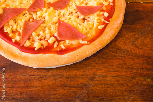 Cheap 12 inch Ham and cheese pizza made with par-baked dough, ham, tomato sauce and processed cheese. On a wood tray. photo