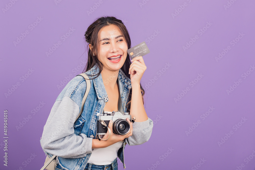 Happy Asian portrait beautiful young woman excited smiling photographer holding debit credit card bank and retro vintage photo camera ready travel isolated on purple background, tourism and vacation Happy Asian portrait beautiful young woman excited smiling photographer holding debit credit card bank and retro vintage photo camera ready travel isolated on purple background, tourism and vacation