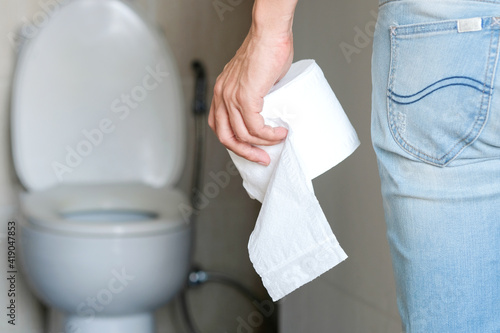 Fototapeta Naklejka Na Ścianę i Meble -  Man's hand, he holds a roll of toilet paper Going to the bathroom Toilet toilet background