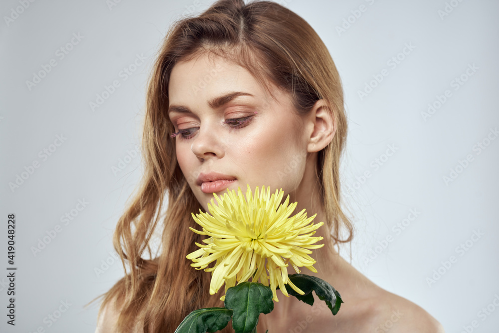 Charming lady with yellow flower on a light background cropped view Charming lady with yellow flower on a light background cropped view