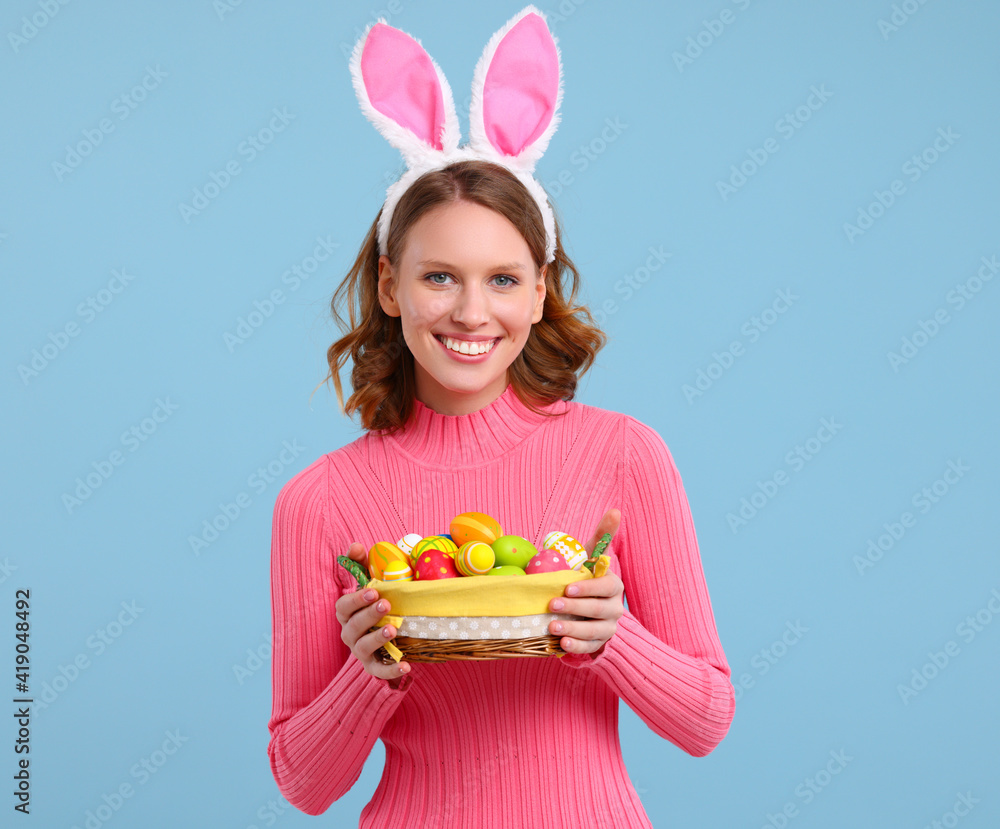 Positive young woman with bunny ears smiling and holding Easter basket in hands Positive young woman with bunny ears smiling and holding Easter basket in hands