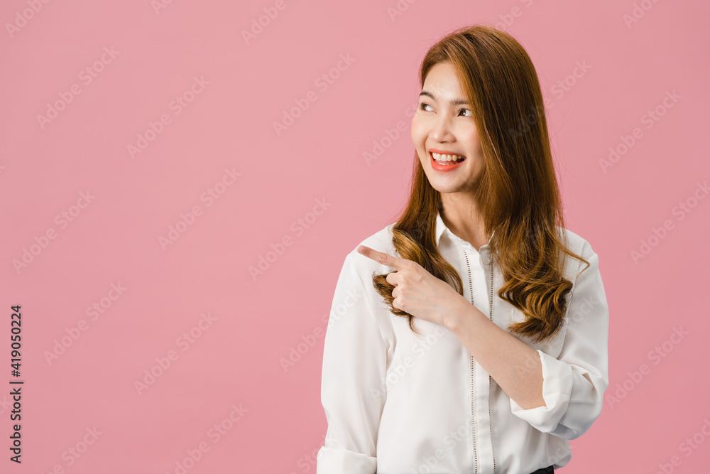 Portrait of young Asian lady smiling with cheerful expression, shows something amazing at blank space in casual clothing and standing isolated over pink background. Facial expression concept. Portrait of young Asian lady smiling with cheerful expression, shows something amazing at blank space in casual clothing and standing isolated over pink background. Facial expression concept.