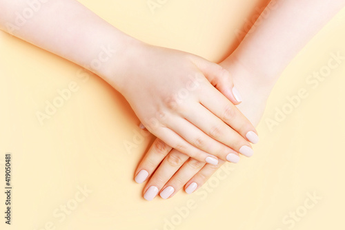 Female hands with a brown manicure on brown background, top view
