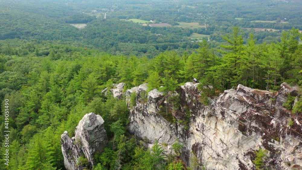 Aerial panning shot of tourists moving down on rocky cliff amidst trees, drone flying over lush forest - Berkshire County, Massachusetts Aerial panning shot of tourists moving down on rocky cliff amidst trees, drone flying over lush forest - Berkshire County, Massachusetts