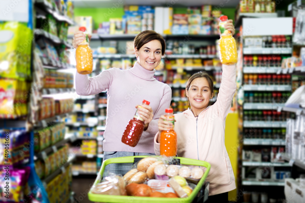 Positive woman customer with girl looking for refreshing beverages in supermarket. Focus on the woman