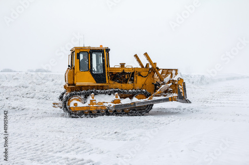 Yellow bulldozer removes snowdrifts in a severe blizzard at winter