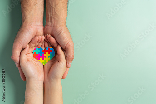 Adult and child hands holding jigsaw puzzle heart shape, World Autism Awareness Day