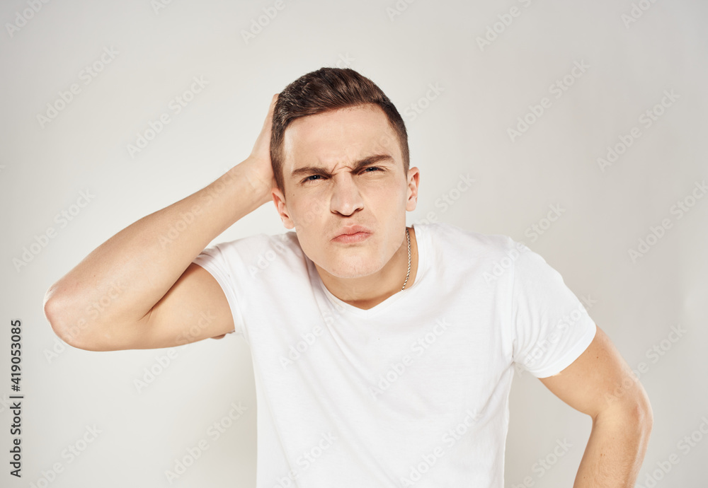 A puzzled man touches himself with his hands on a light background in a white T-shirt A puzzled man touches himself with his hands on a light background in a white T-shirt