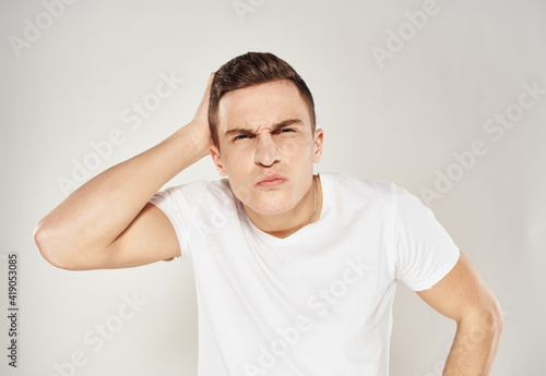 A puzzled man touches himself with his hands on a light background in a white T-shirt