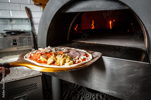 Fresh original Italian raw pizza, preparation in traditional style. Restaurant chef takes pizza from oven in traditional restaurant