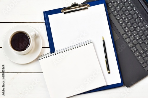Notepad, clipboard on laptop with cup coffee and pen on wood white background. Workplace. copy space, flat lay. Concept business and finance.