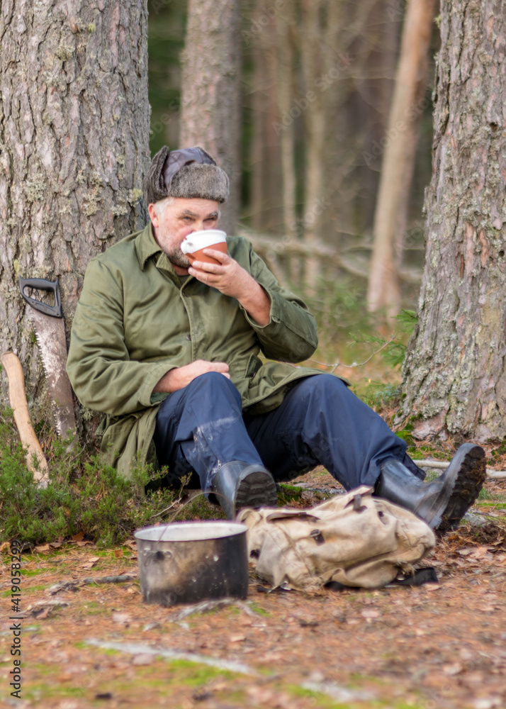 a forester in the forest drinks tea at rest, blurred forest background, bonfire with a pot over it, in the autumn