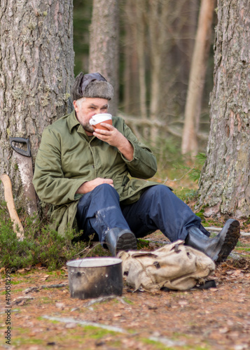 a forester in the forest drinks tea at rest, blurred forest background, bonfire with a pot over it, in the autumn