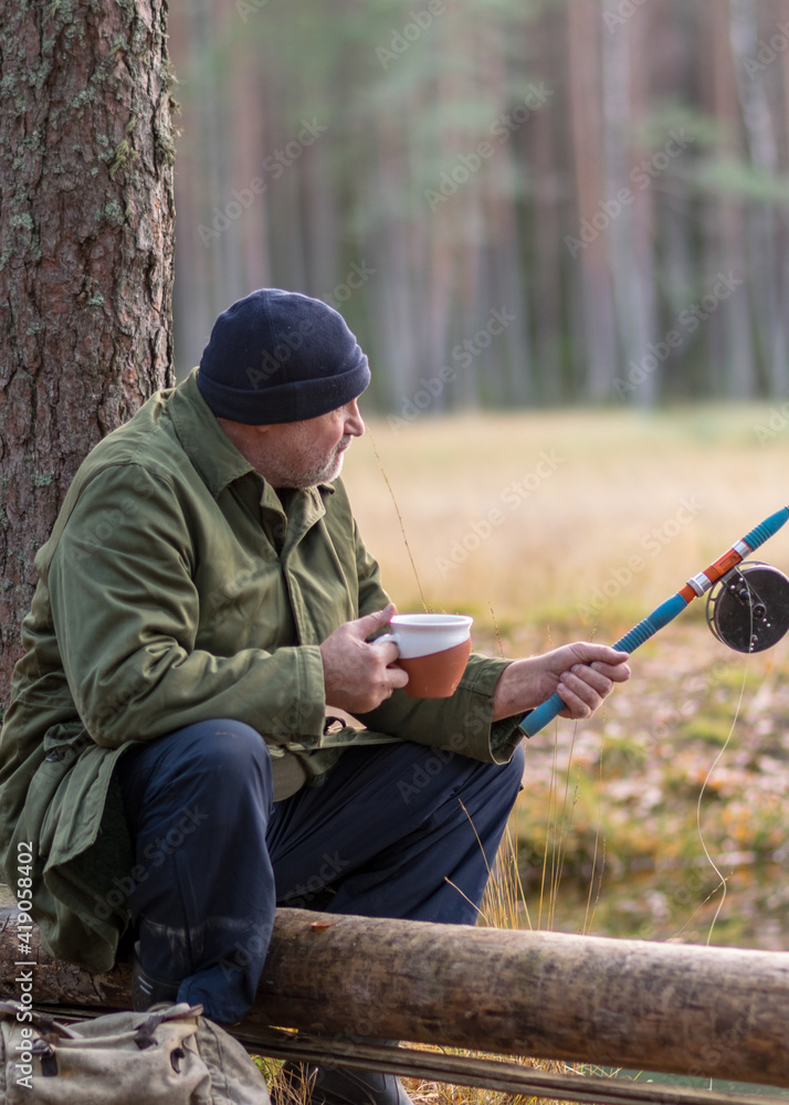 Naklejka premium fisherman by the river sits on a tree branch and drinks tea, blurred tree background, autumn