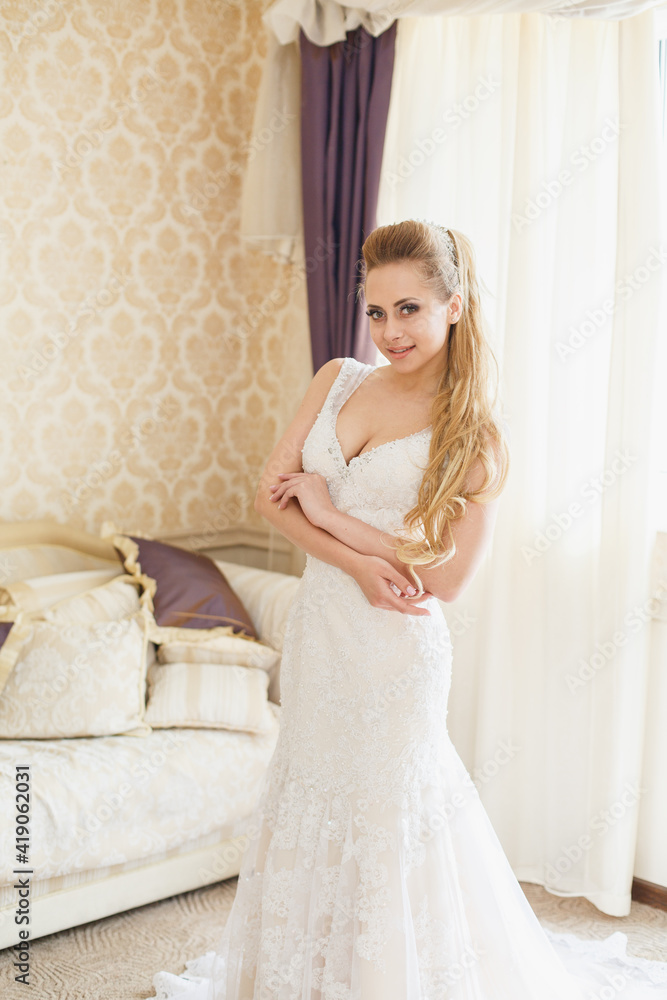 Pretty young Bride in wedding dress. Blonde-haired woman with wedding hair-style with a long tail. Boudoir morning of the bride.
