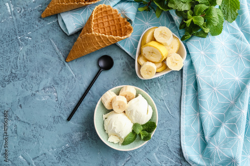 Bowl with tasty banana ice-cream and waffle cones on color background