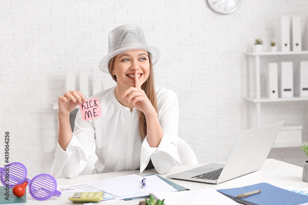 Young businesswoman holding sticky note with text KICK ME at workplace in office. April Fools Day celebration Young businesswoman holding sticky note with text KICK ME at workplace in office. April Fools Day celebration