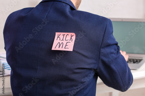 Sticky note with text KICK ME on back of man working in office. April Fools Day celebration